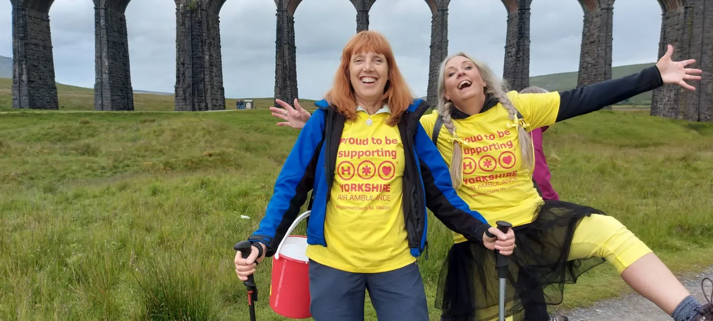 Two walkers with yellow t-shirts with the Ribblehead viaduct behind them.