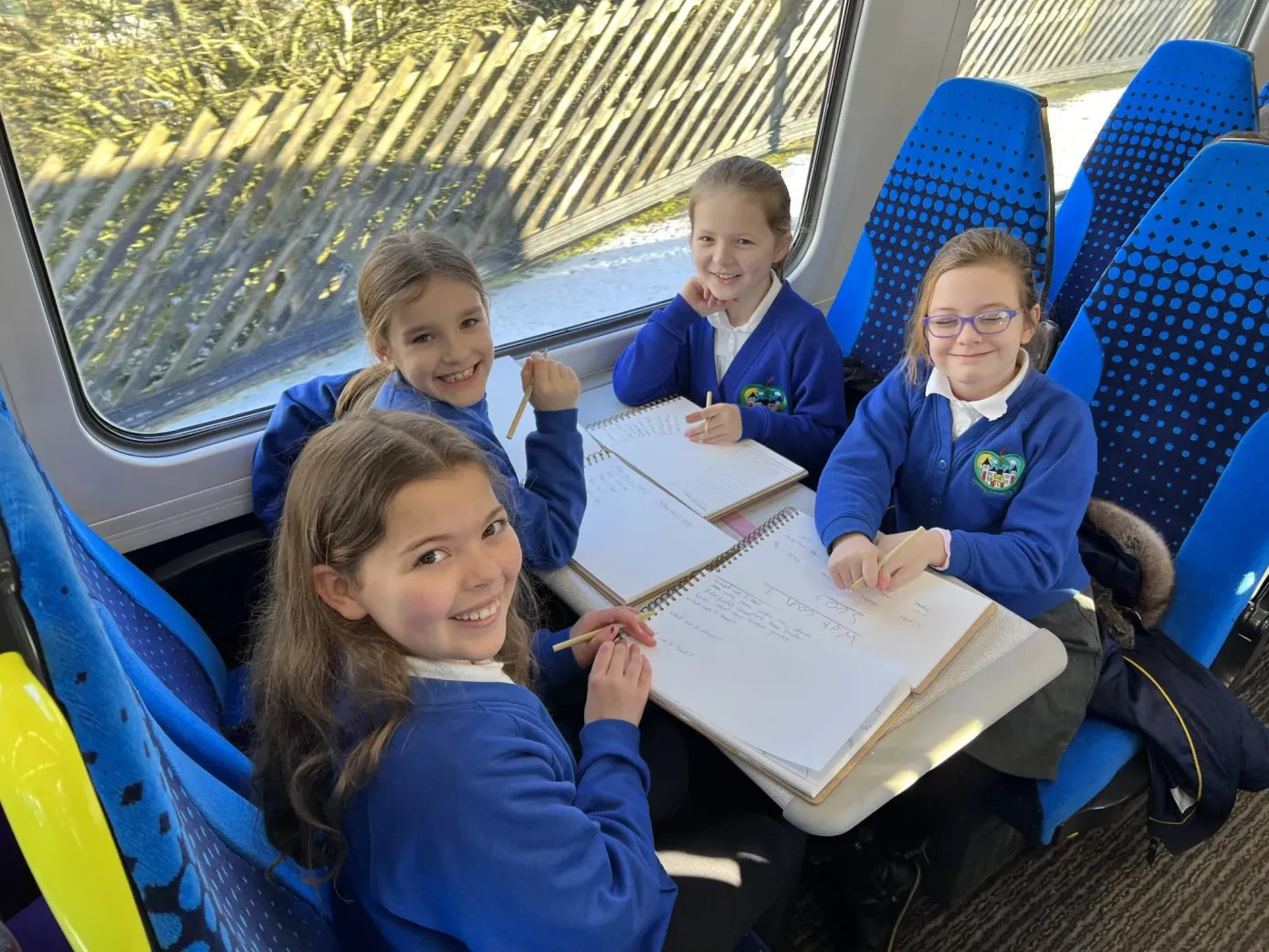Four school pupils sat around table on train with sketch books