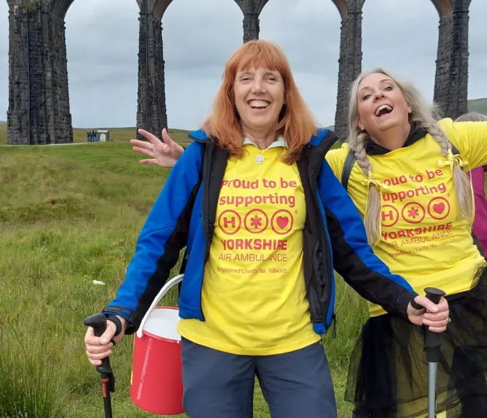 Two walkers with yellow t-shirts with the Ribblehead viaduct behind them.