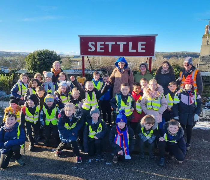 Full class from Appleby Primary School sat in front of the Settle station sign