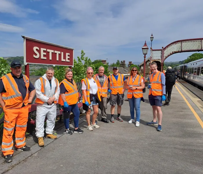 A group of people in hi-vis with the sign Settle next to a railway line and footbridge