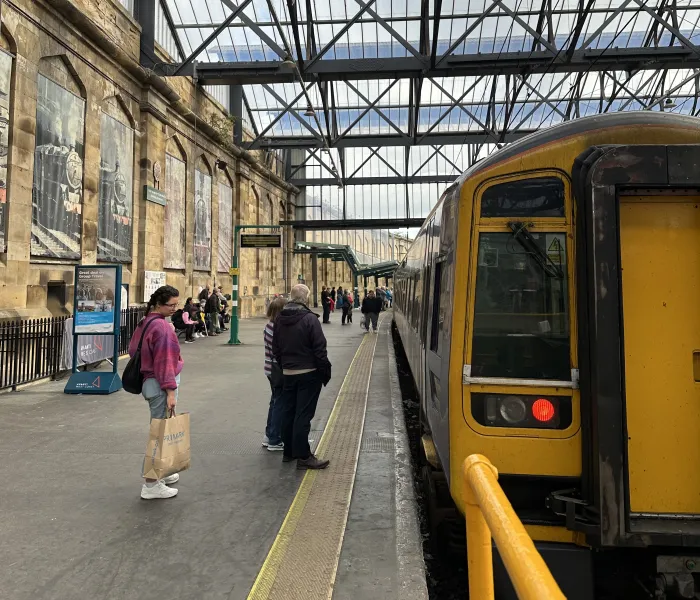A diesle train at the platfrom with two people waiting to get on
