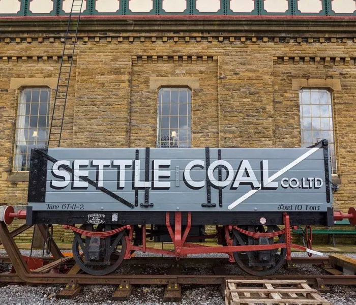 A railway truck infornt of a water town, with the words Settle Coal painted on the side