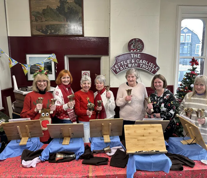 7 women with hand bells in a train station waiting room