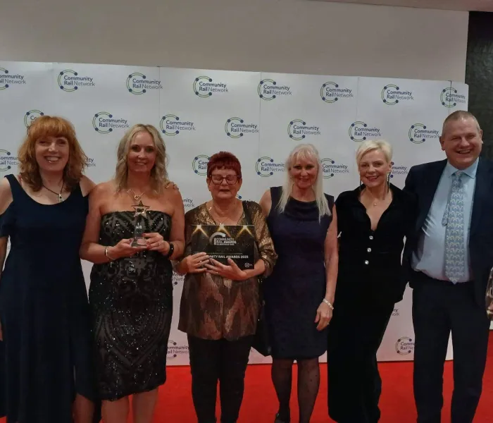 5 woman and one man with an award infrom of banner saying Community Rail Awards 2025