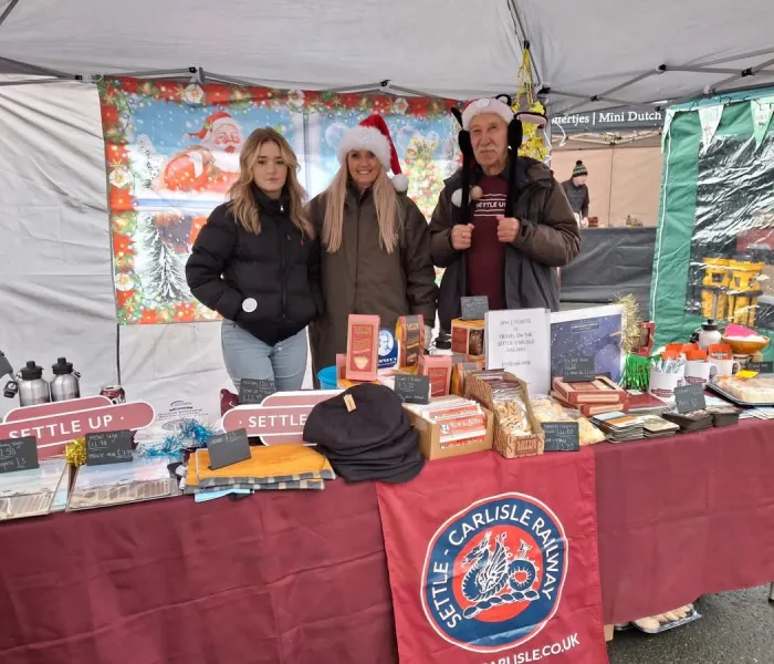 Three people, with santa hats on a stall with Settle Carlisle Railway logo