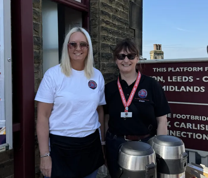 a blond woman and a brunette woman at a drinks stall outside a station