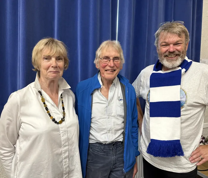 A woman and two men stood infront of a blue curtain, one man wething a blue and white Halifax Town football scarf