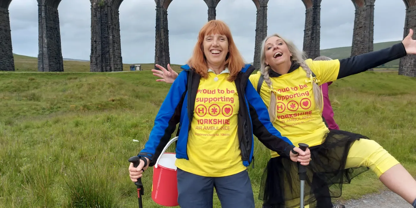 Two walkers with yellow t-shirts with the Ribblehead viaduct behind them.