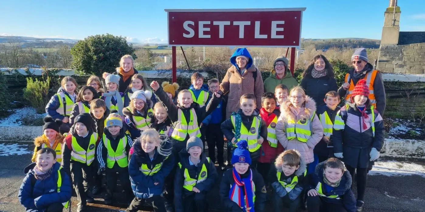 Full class from Appleby Primary School sat in front of the Settle station sign