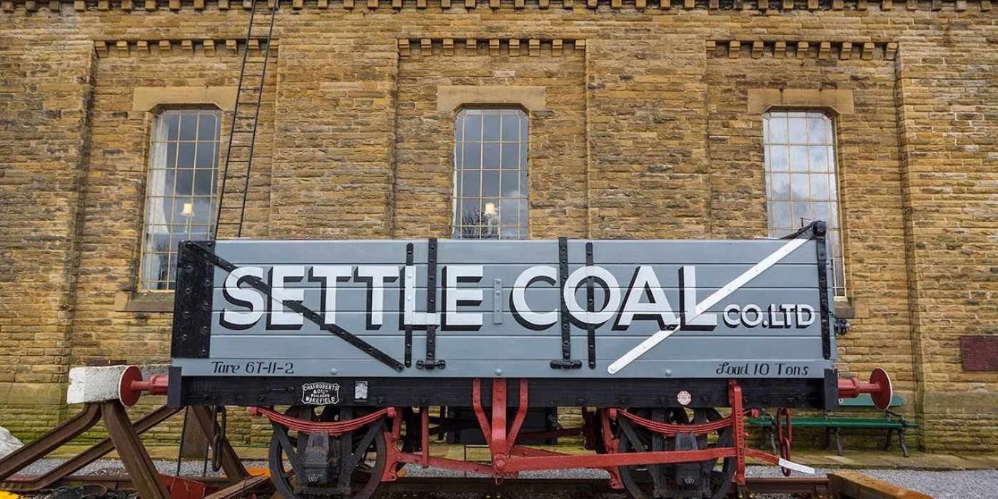 A railway truck infornt of a water town, with the words Settle Coal painted on the side