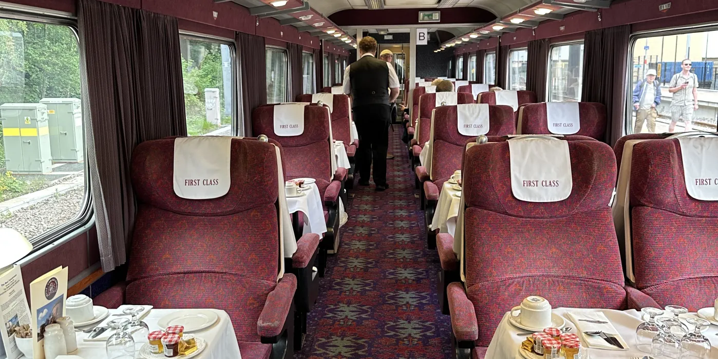 A railway carriage set up for breeakfast with white table cloths.
