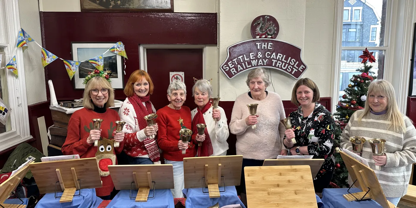 7 women with hand bells in a train station waiting room