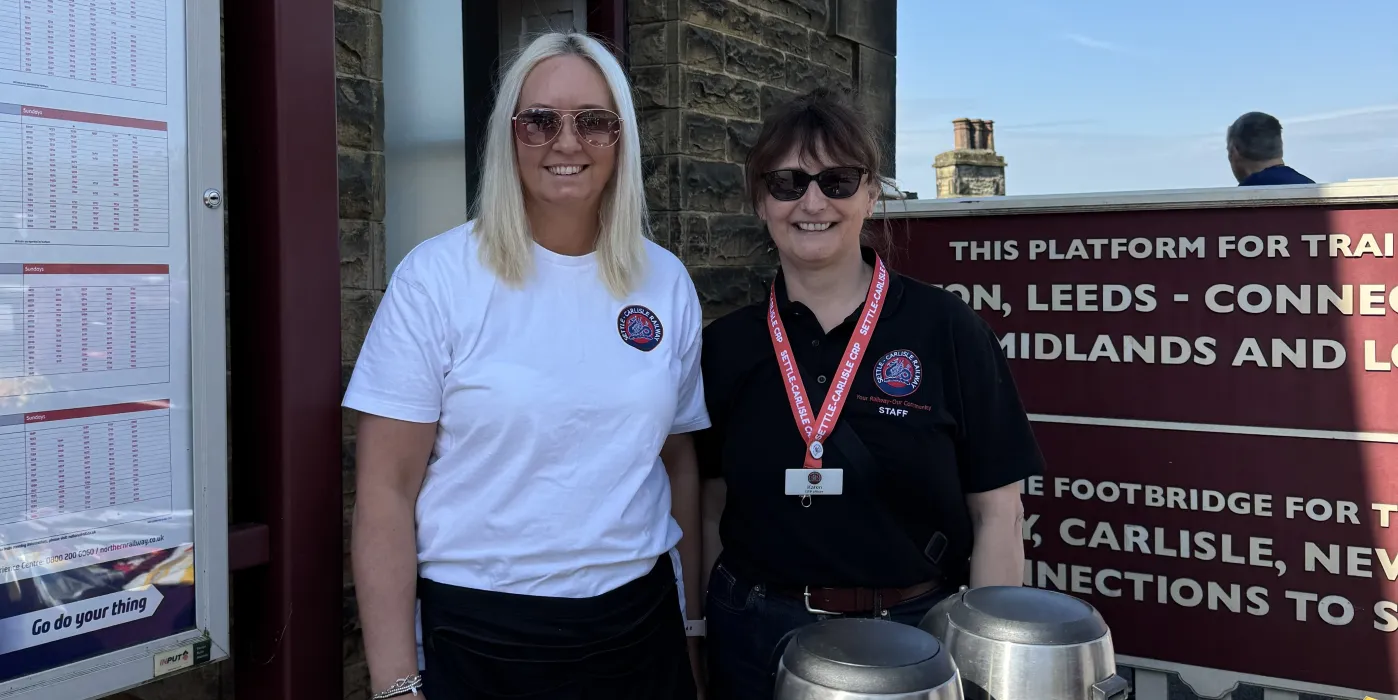 a blond woman and a brunette woman at a drinks stall outside a station