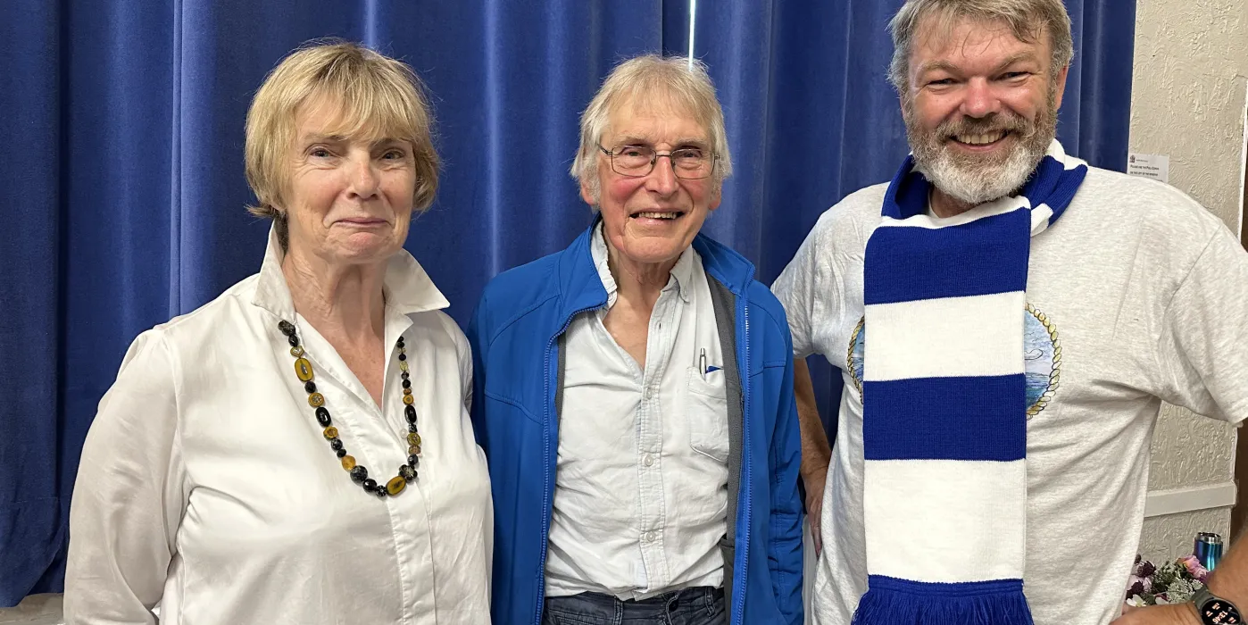 A woman and two men stood infront of a blue curtain, one man wething a blue and white Halifax Town football scarf